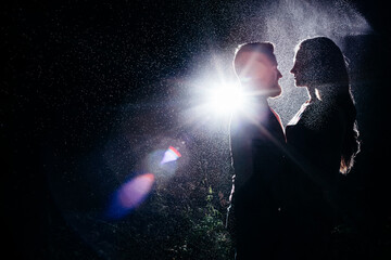 A couple in love stands opposite each other in the rain, raindrops in the backlight. Silhouettes of a couple, portrait.  Love, love story, valentine's day.