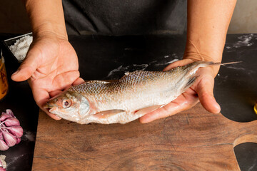 a chef dressed in a black apron, holding a fresh fish