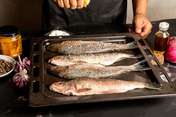 A cook placing salt on fresh fish in a metal cooking tray.