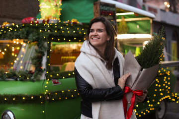 Happy woman with thuja tree near Christmas bus outdoors. Space for text