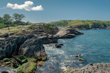 Beach at Forte São Mateus in Cabo Frio at the end of the afternoon, with many mountains around and some people fishing from boats or on the rocks.