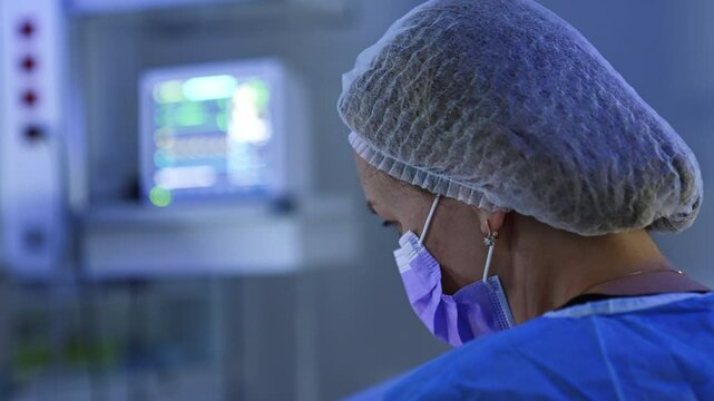 Rear view of the head of female doctor in mask and cap. Medic looks down at the operating spot. Close up.