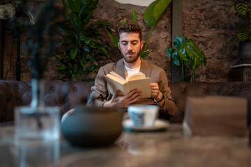 Man reading a book in coffee shop with tea on table, cozy atmosphere