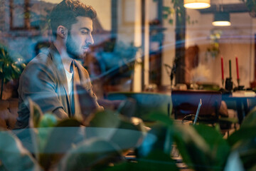 Man working on laptop with city reflections on coffee shop window