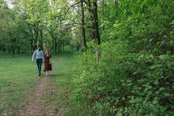 A couple in love walks hand in hand through a park with green trees, love story, Valentine's day, holiday, park, forest, nature, engagement.