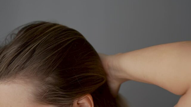 Young blonde woman showing receding hairline on her forehead and temples pushing hair back with her hand. Hair care. A girl demonstrating a healthy scalp and the absence of dandruff. Slow motion