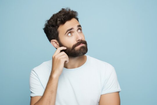 Young Man Biting Nails. Portrait of Confused Adult Guy in Casual T-Shirt, Isolated on Pastel Blue Background. People Lifestyle Concept