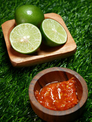 Closeup Traditional Indonesian food, sambal terasi and fresh lime served in a wooden bowl with a green synthetic grass base.