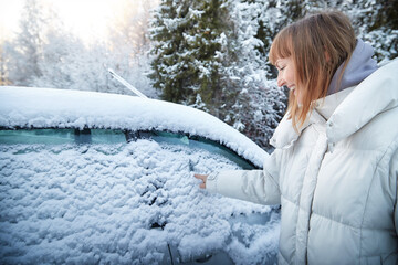 Woman enjoying a snowy day while clearing frost from her car on a winter morning