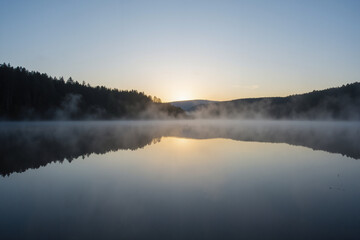 Serene lake at sunrise with mist and forest reflection