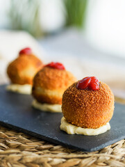 Close-up of golden, breaded ham croquettes served on a slate plate, topped with tomato sauce and mayonnaise base.