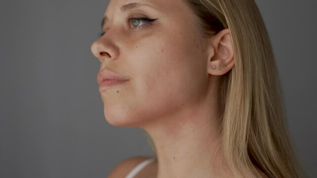 Young caucasian blonde woman runs her hand over her chin and neck on a dark grey background. Mentoplasty plastic surgery concept