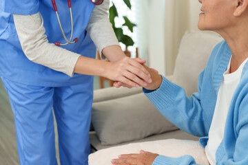 Close-up of nurse gently holding elderly woman’s hand during home care session. Emphasizes...