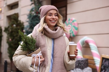 Happy woman with thuja tree and paper cup of coffee on city street. Christmas season
