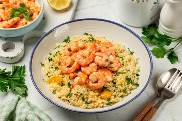 Plate with Couscous and fried Shrimps, yellow tomatoes, onion, parsley.  Close up. White table surface.