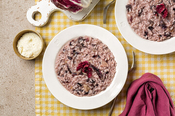 Italian risotto with radicchio rosso and cheese in a white plate. Beige table, yellow napkin. Top view.