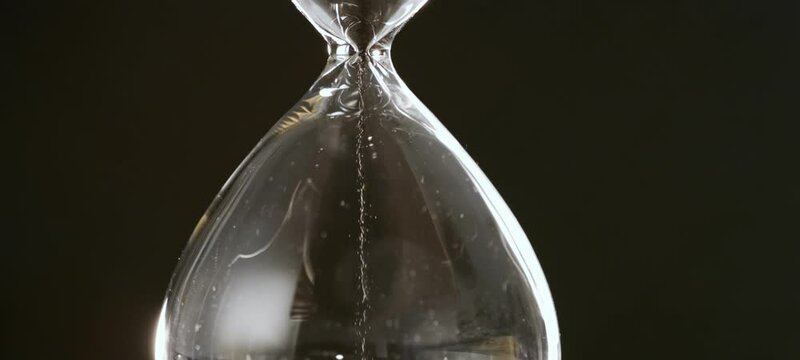 Extreme close-up view of sand flows through an hourglass in slow-motion.