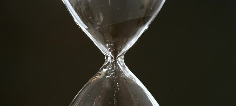 Sand running through the bulbs of an hourglass, measuring the passing time in a countdown to a deadline. Slow-motion footage