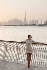 A beautiful tourist woman in a white dress enjoys the panoramic sunset view of the Dubai skyline, UAE