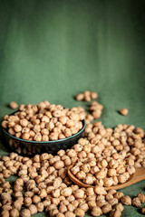 Rustic close-up of dried chickpeas in a wooden spoon and a bowl on a green fabric background. Natural light highlights textures, perfect for healthy food, vegan recipes, and organic lifestyle concepts