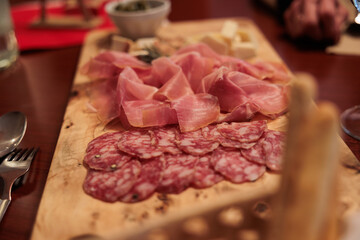 tagliere di legno con vari salumi affettati, come prosciutto cotto e salame e formaggi, su un tavolo