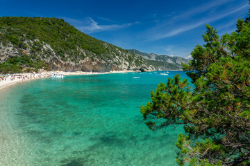 People and boats at Cala Luna beach and clear transparent blue water in the Gulf of Orosei,...