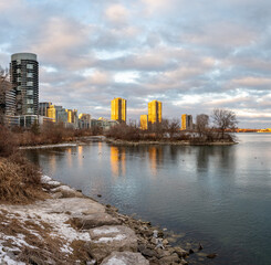 Obraz premium Golden hour sunset illuminates a cityscape reflected in tranquil waters, showcasing modern high-rise buildings juxtaposed against a serene natural landscape. downtown toronto lakeshore mimic