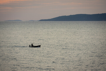 Naklejka premium silhouette lone boat cuts through the calm waters as the sun begins its descent, casting a warm glow across the horizon