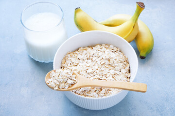 Oat flakes in bowl, milk and bananas on blue background