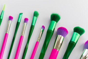 Spring must have beauty purchase concept. Green and pink makeup brushes over white background 