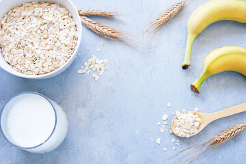 Oat flakes in bowl, milk and bananas on blue background
