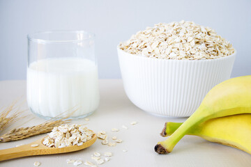 Oat flakes in bowl, milk and bananas on white table