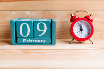 February 9. Blue cube calendar with month and date on wooden background.