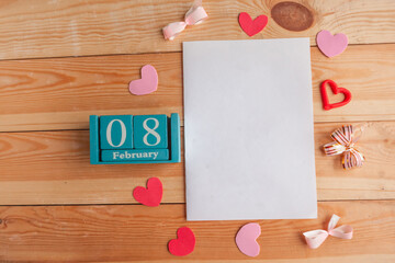 February 8. Blue cube calendar with month and date and white mockup blank on wooden background.