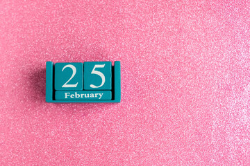 February 25. Blue cube calendar with month and date on pink glitter background. Copy space for the...