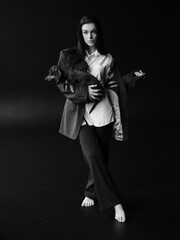 Young woman poses at full height and holding dachshund dog in her hands against black background.