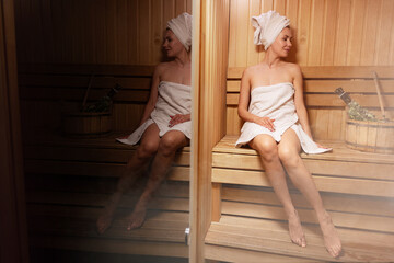 Young woman relaxing and sweating in hot sauna wrapped in towel. Girl In Sauna. Interior of Finnish sauna, classic wooden steam room with hot steam. Russian bathroom. Relax in hot Bathhouse with steam