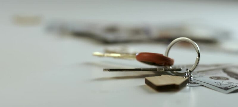 Home keys with wooden house shaped keychain falling on the table in slow motion. Close-up shot