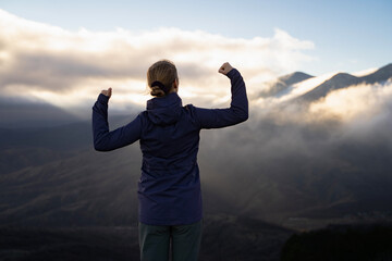 A female hiker with her hands up stands on top of the mountain. Successful woman honor of reaching the top of a mountain during a hiking trip.. Celebration of victory. Achievement of goals.