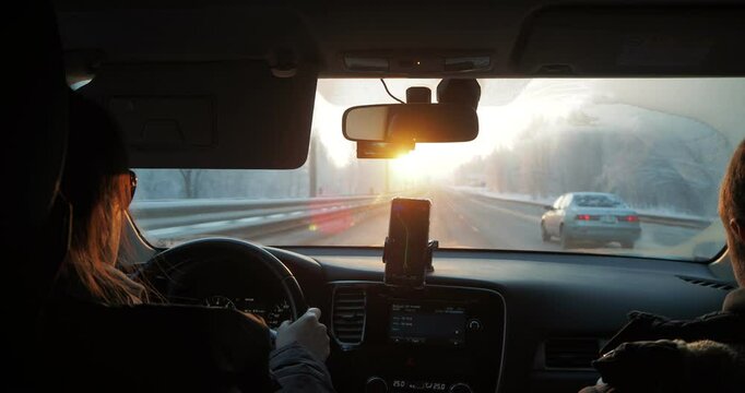 Transport. A woman drives a car on a winter road using the navigator in her phone moving towards the sun. Hand held.