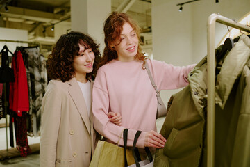 Medium close up of brunette and red haired best friends looking at khaki jacket from brand new...