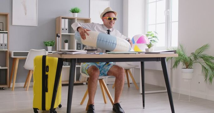 Happy funny business man in swim ring at table in office workplace books holiday online, finishes work, closes laptop computer, moves arms like plane wings all set and ready for summer travel vacation