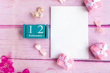 February 12. Blue cube calendar with month and date and white mockup blank on pink background.