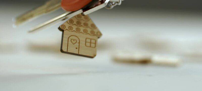 Slow-motion shot of two house keys with a house shaped keychain falling on the table in blurr background