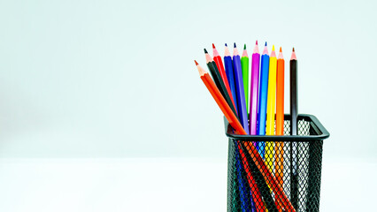 Close-up set of colored pencils in a metal black basket over. can with pencils. Space for text