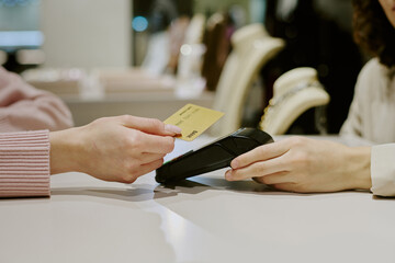 Medium close up of unrecognizable woman tapping golden card while hand of seller holding payment terminal