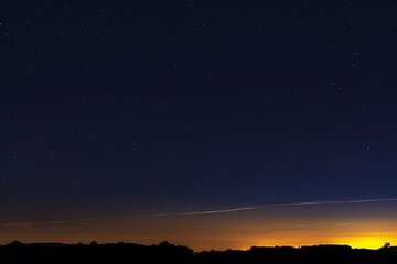 Naklejka premium Silhouetted trees against a vibrant twilight sky. Orange and yellow hues meet the dark night, dotted with stars. A subtle atmospheric layer is visible.