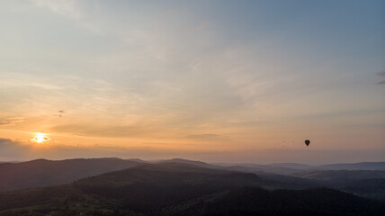 Obraz premium Majestic Mountains, Dense Green Forests, And Dramatic Clouds Illuminated By A Stunning Sunset. Aerial View Capturing The Breathtaking Beauty Of Nature From Above.