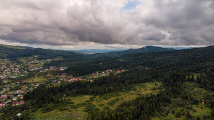 Obraz premium Aerial View Of A City Surrounded By Majestic Mountains Under A Cloudy Sky. The Dramatic Landscape Creates A Stunning Contrast Between Urban Life And Natural Beauty.