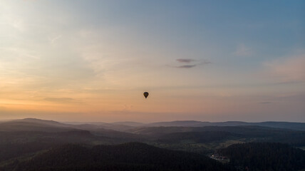 Aerial View Of Majestic Mountains Shrouded In Clouds And Mist, Overlooking Expansive Agricultural Fields And A Quaint Small Town, Capturing The Serene Beauty Of The Countryside.